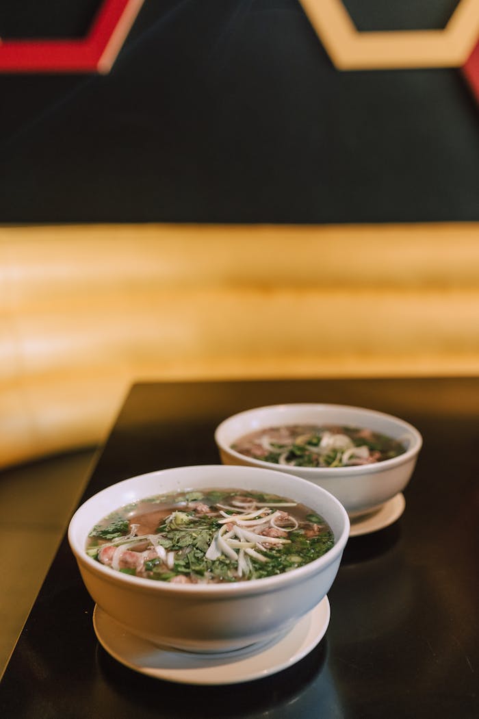 Two bowls of traditional Vietnamese pho soup on a table indoors.